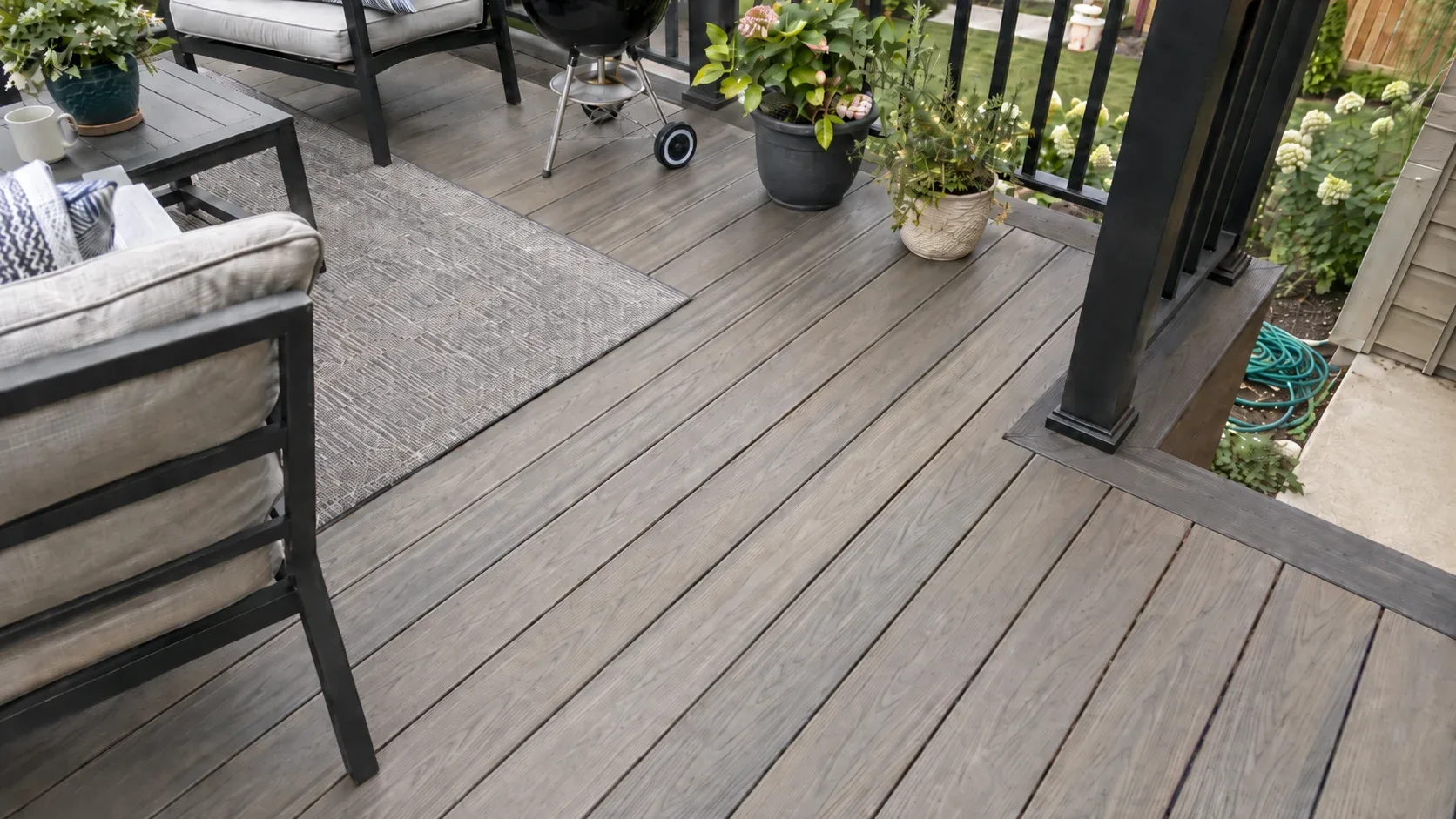 A close view of capped composite decking with embossed woodgrain, a contrasting picture frame border board and an aluminium railing post base, with no fasteners showing in the field